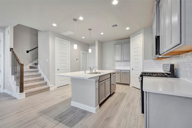 kitchen featuring sink, gray cabinetry, hanging light fixtures, stainless steel appliances, and a kitchen island with sink