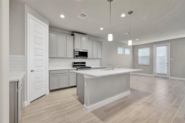 kitchen with sink, gray cabinetry, decorative light fixtures, appliances with stainless steel finishes, and a kitchen island with sink