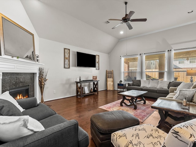 living room with dark wood-type flooring, a tile fireplace, vaulted ceiling, ceiling fan, and ornamental molding