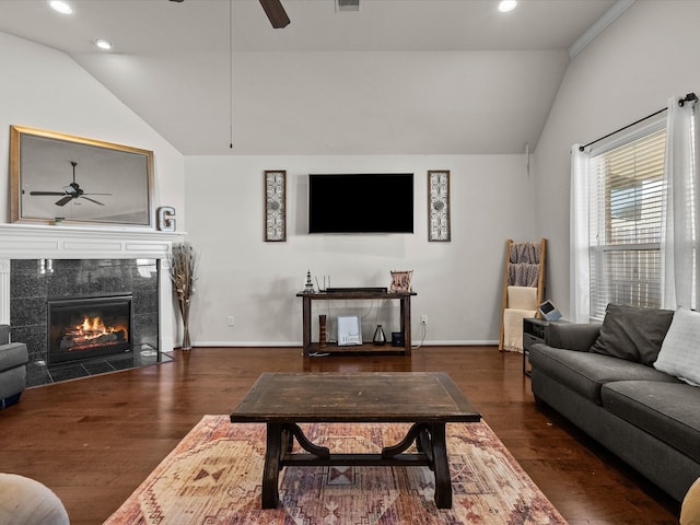 living room with ceiling fan, dark wood-type flooring, a tile fireplace, and vaulted ceiling