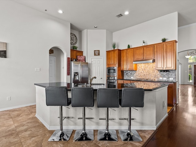 kitchen featuring a high ceiling, stainless steel appliances, a breakfast bar area, and an island with sink