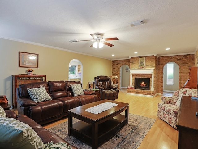 living room with ceiling fan, ornamental molding, light hardwood / wood-style flooring, and a brick fireplace