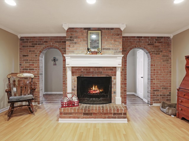 living room with crown molding, wood-type flooring, and a brick fireplace