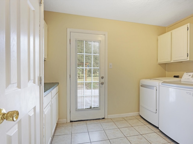 clothes washing area with washing machine and dryer, light tile patterned floors, and cabinets