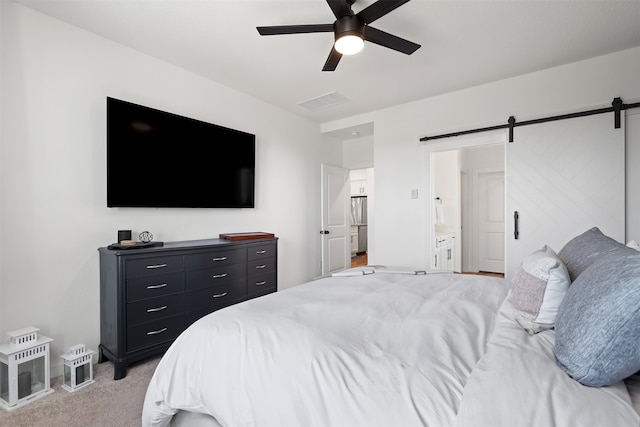 bedroom featuring connected bathroom, stainless steel fridge, a barn door, light colored carpet, and ceiling fan