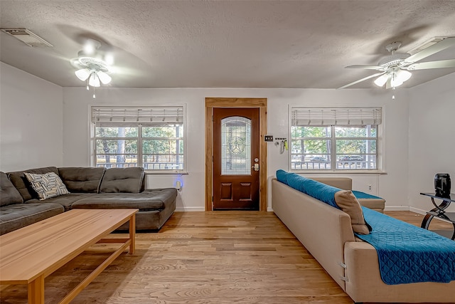 living room featuring a textured ceiling, light wood-type flooring, a wealth of natural light, and ceiling fan