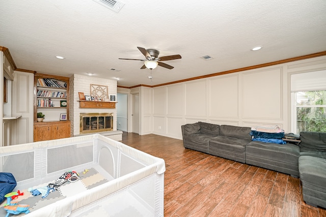 living room with a large fireplace, ceiling fan, a textured ceiling, hardwood / wood-style flooring, and ornamental molding