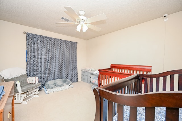 bedroom with a textured ceiling, a crib, carpet, and ceiling fan