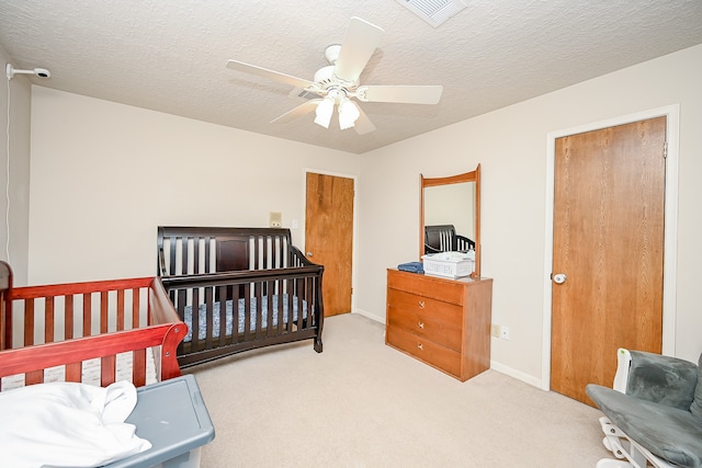 bedroom featuring light carpet, a textured ceiling, a crib, and ceiling fan