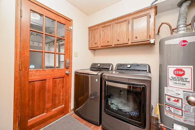 clothes washing area featuring separate washer and dryer, a textured ceiling, water heater, hardwood / wood-style floors, and cabinets