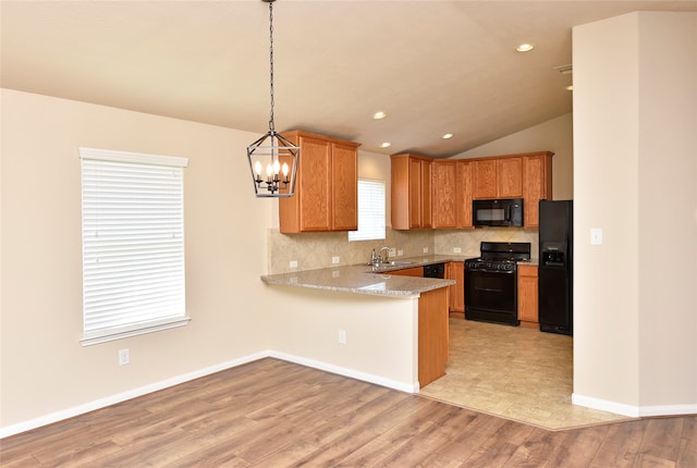 kitchen with black appliances, sink, kitchen peninsula, pendant lighting, and light hardwood / wood-style flooring