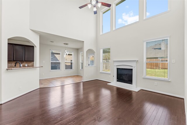 unfurnished living room with a towering ceiling, a healthy amount of sunlight, light wood-type flooring, and ceiling fan