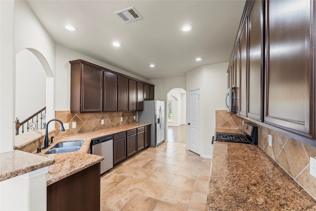 kitchen featuring appliances with stainless steel finishes, sink, dark brown cabinets, light stone counters, and decorative backsplash