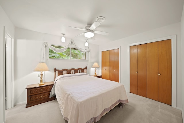 carpeted bedroom with ceiling fan and two closets