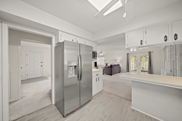 kitchen with appliances with stainless steel finishes, french doors, light carpet, tile counters, and white cabinets