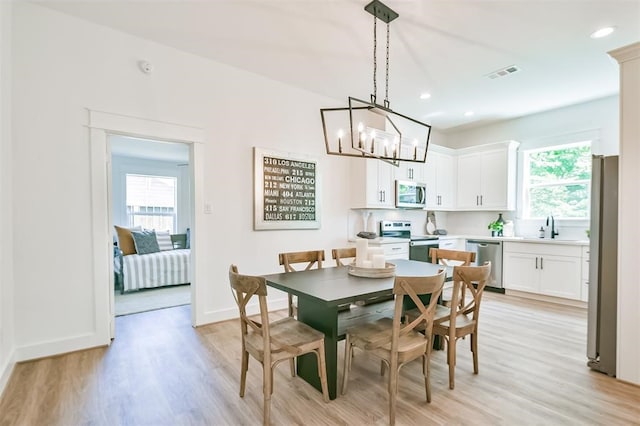 dining area with light wood-type flooring, sink, plenty of natural light, and a chandelier