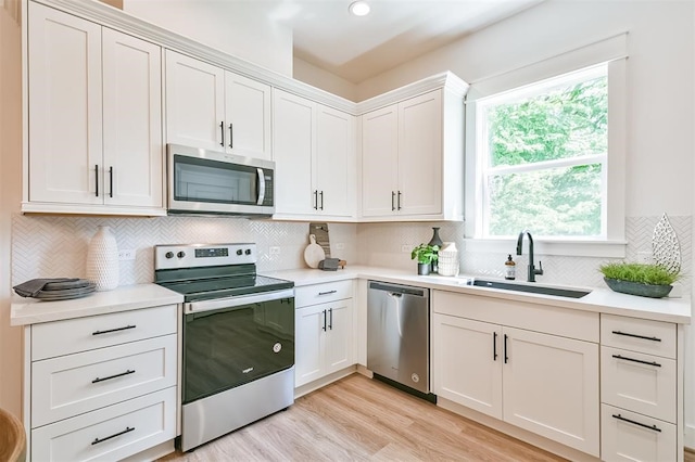 kitchen with sink, backsplash, white cabinetry, light hardwood / wood-style floors, and stainless steel appliances