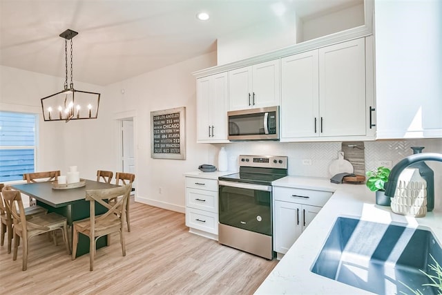 kitchen featuring appliances with stainless steel finishes, white cabinetry, light wood-type flooring, sink, and decorative light fixtures