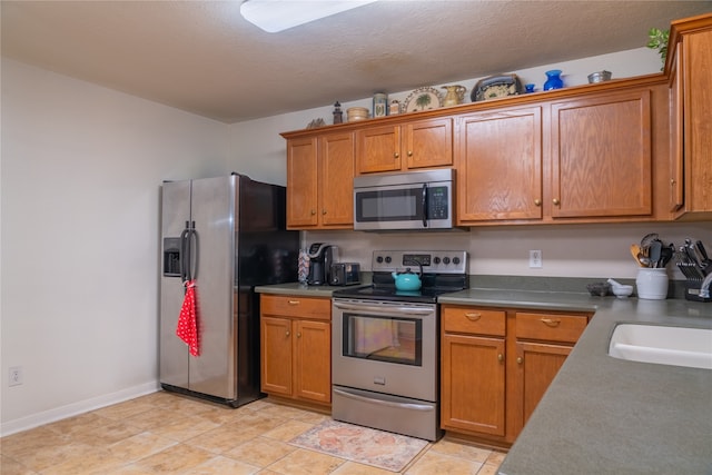 kitchen with appliances with stainless steel finishes, a textured ceiling, sink, and light tile patterned floors