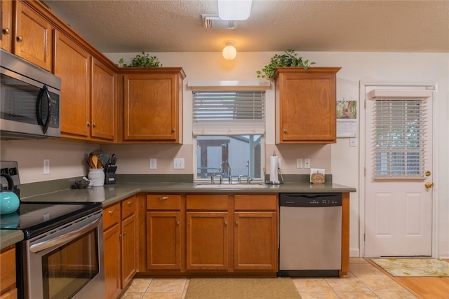 5618 Tiger Lilly Way, Houston, TX 77085 - kitchen featuring appliances with stainless steel finishes, a sink, brown cabinetry, dark countertops, and a textured ceiling