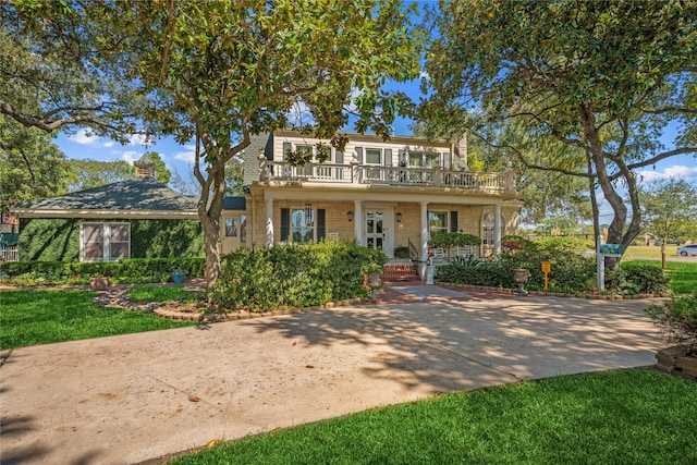 view of front property featuring a balcony, covered porch, a front yard, and brick siding