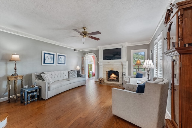 living room featuring a fireplace, a textured ceiling, ceiling fan, and crown molding