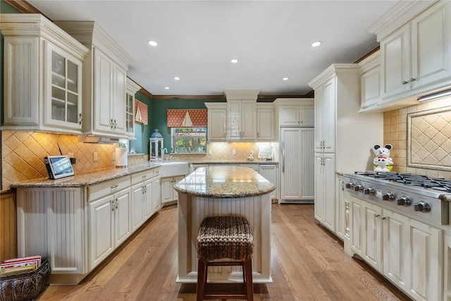 kitchen with paneled built in fridge, a center island, light stone countertops, glass insert cabinets, and stainless steel gas stovetop