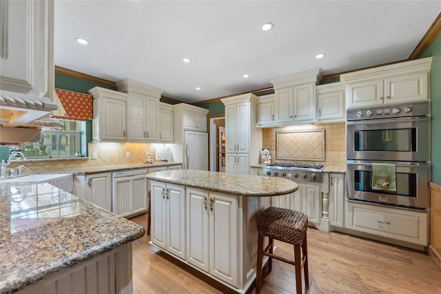 kitchen featuring light wood-style flooring, appliances with stainless steel finishes, a center island, crown molding, and a sink