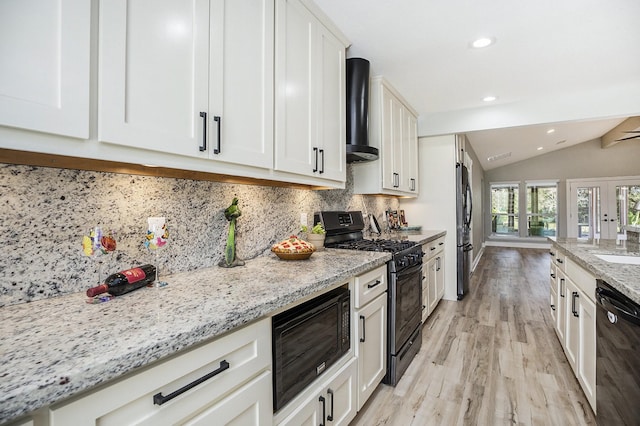 kitchen featuring lofted ceiling, black appliances, wall chimney exhaust hood, light stone countertops, and light hardwood / wood-style floors