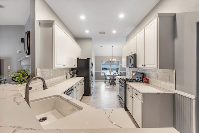 kitchen featuring white cabinets, appliances with stainless steel finishes, light stone countertops, pendant lighting, and sink