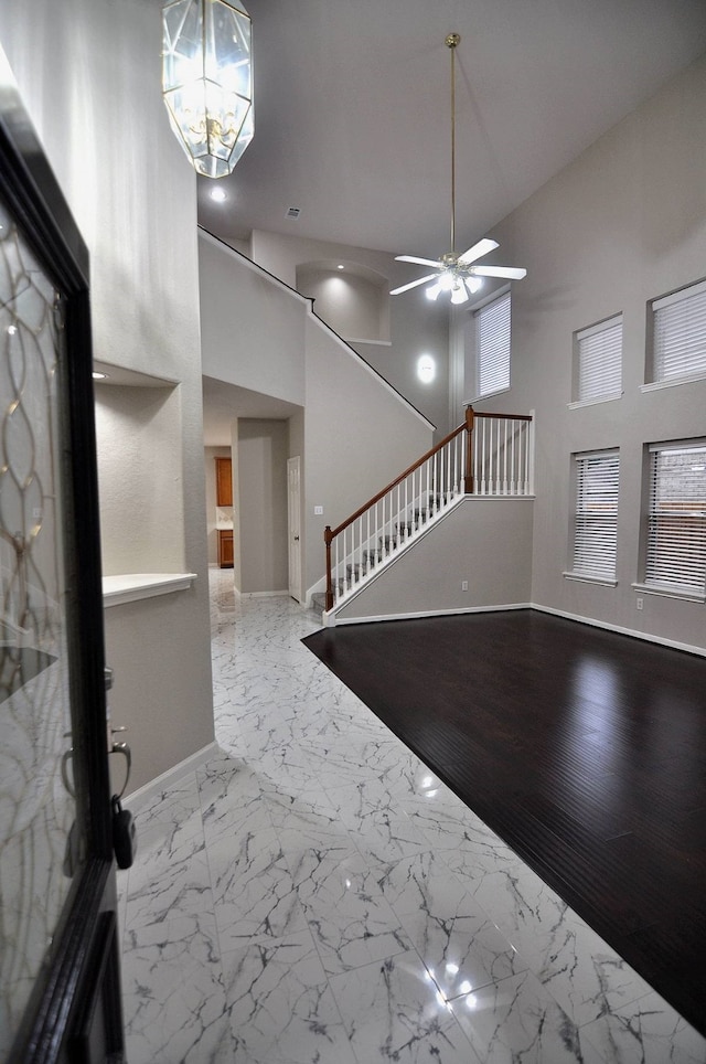 entrance foyer with a towering ceiling, ceiling fan with notable chandelier, and hardwood / wood-style floors