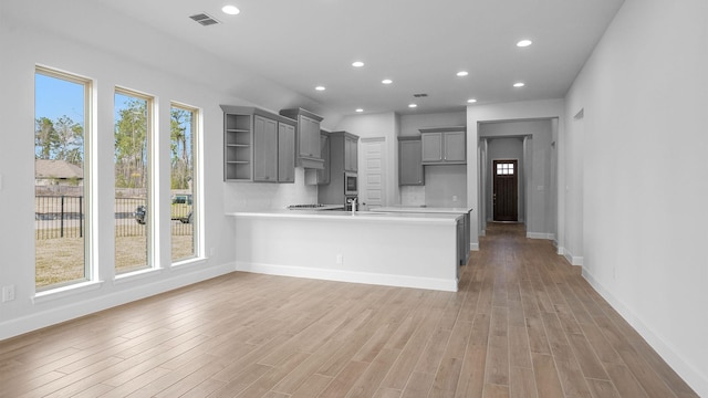 kitchen with wood-type flooring, gray cabinets, kitchen peninsula, and a healthy amount of sunlight