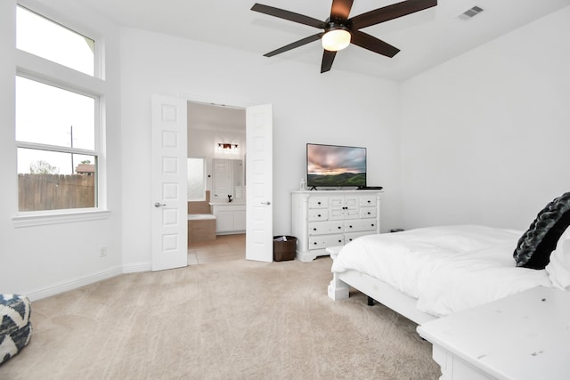 bedroom with ensuite bathroom, light colored carpet, and ceiling fan