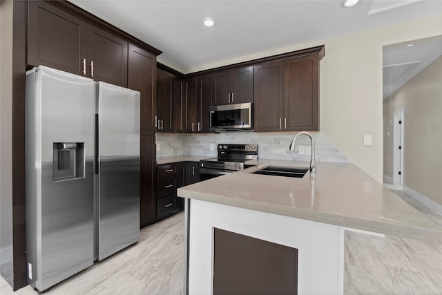 kitchen with kitchen peninsula, backsplash, sink, dark brown cabinetry, and appliances with stainless steel finishes