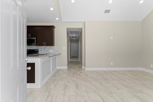 kitchen featuring kitchen peninsula, tasteful backsplash, dark brown cabinets, black range oven, and sink