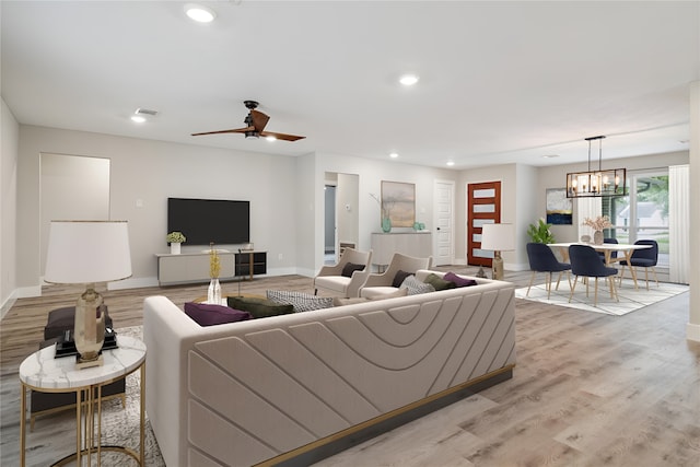 living room with light hardwood / wood-style floors and ceiling fan with notable chandelier