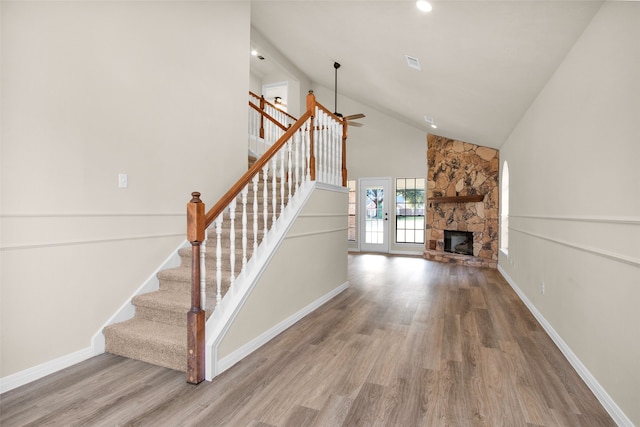 staircase with wood-type flooring, high vaulted ceiling, a stone fireplace, and ceiling fan