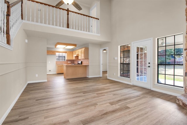 unfurnished living room featuring a high ceiling, light hardwood / wood-style floors, and ceiling fan