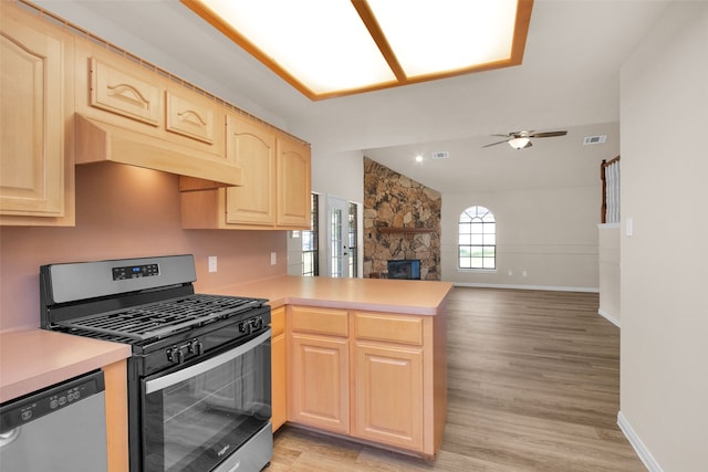 kitchen with kitchen peninsula, appliances with stainless steel finishes, light brown cabinets, light hardwood / wood-style flooring, and a stone fireplace