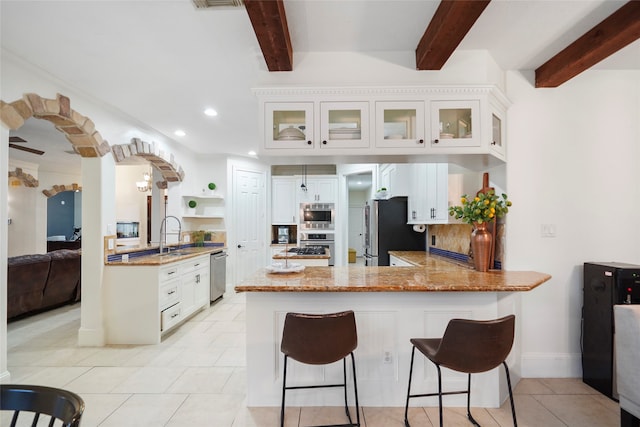 kitchen with appliances with stainless steel finishes, kitchen peninsula, white cabinetry, and beamed ceiling