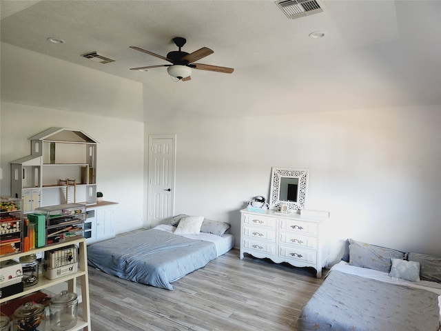 bedroom featuring lofted ceiling, a textured ceiling, light wood-type flooring, and ceiling fan