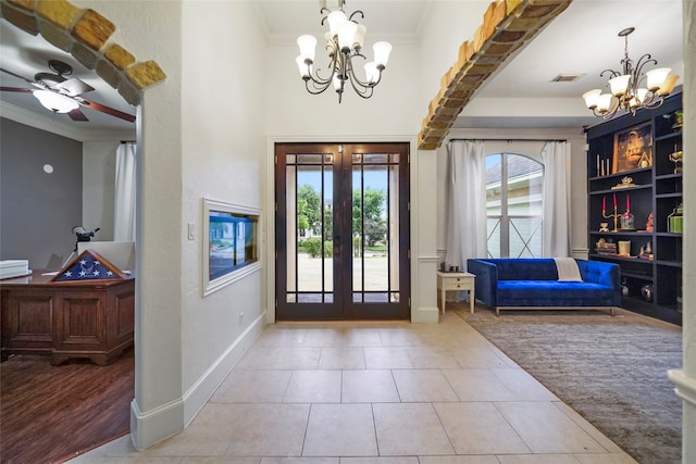 entryway featuring crown molding, ceiling fan with notable chandelier, french doors, and light tile patterned floors