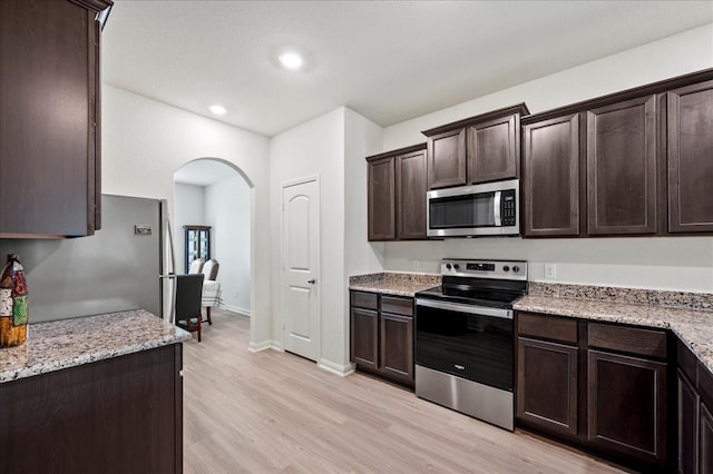 kitchen with appliances with stainless steel finishes, dark brown cabinetry, light stone counters, and light hardwood / wood-style floors