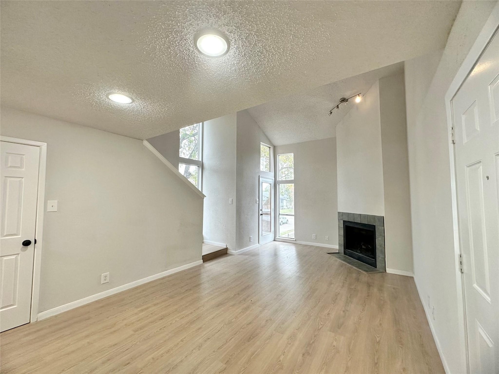 unfurnished living room featuring a tile fireplace, light hardwood / wood-style floors, lofted ceiling, track lighting, and a textured ceiling