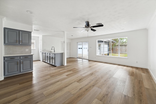 unfurnished living room with light hardwood / wood-style floors, sink, and ceiling fan