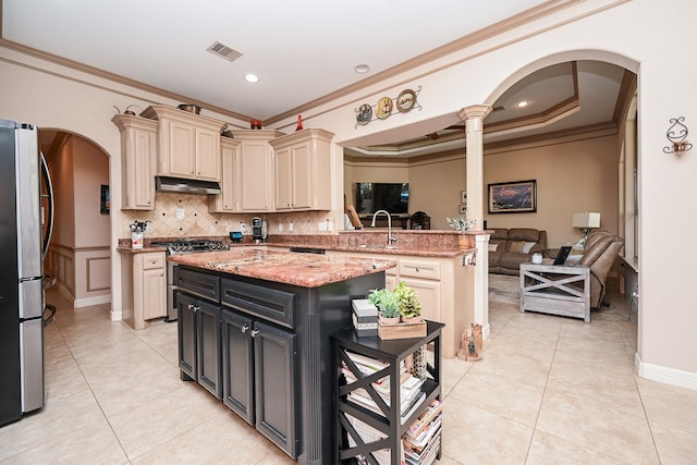 kitchen featuring cream cabinets, ornamental molding, a kitchen island, light stone counters, and stainless steel appliances