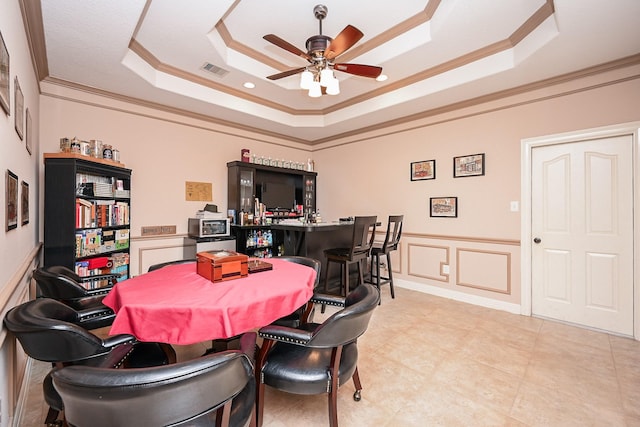 dining area with ceiling fan, a raised ceiling, crown molding, and indoor bar