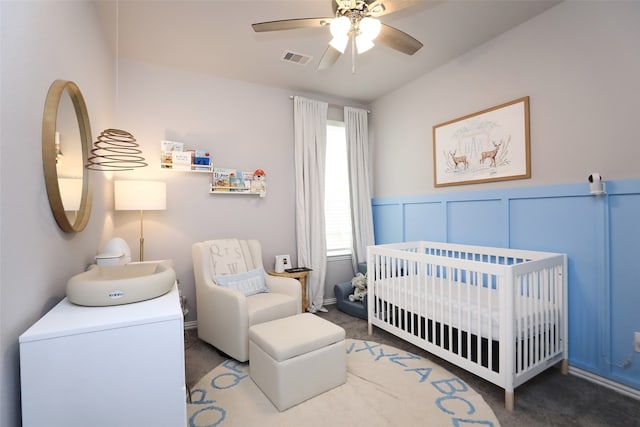 carpeted bedroom with ceiling fan and a nursery area