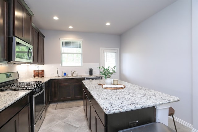 kitchen with stainless steel appliances, backsplash, sink, a center island, and light stone counters