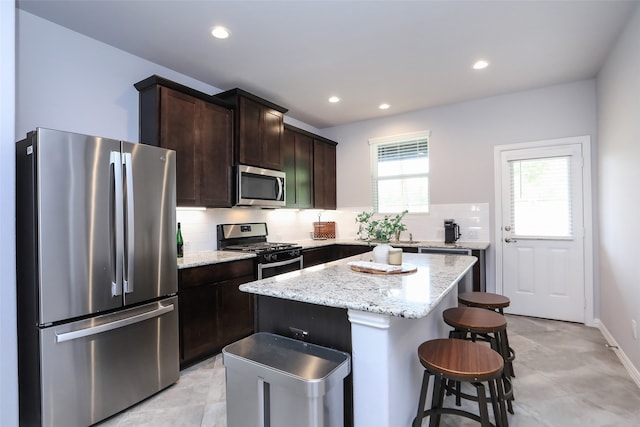 kitchen featuring appliances with stainless steel finishes, light stone countertops, backsplash, and a kitchen island